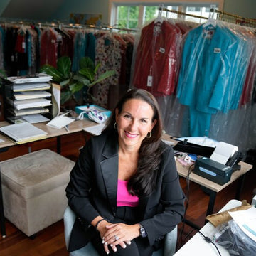 Woman sitting in a clothing store with racks of clothes and office equipment in the background.